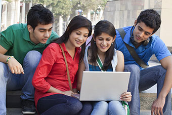 Students on a bench outside discussing around a laptop