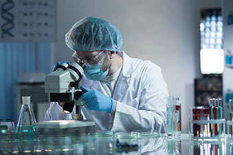 A person, in a lab, looking through a microscope