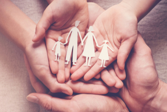 A family resting their open hands on each other whilst holding a paper cut out of a family