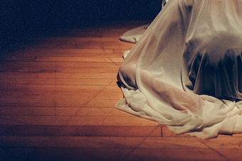 A performer covered in a white sheet laying on the floor
