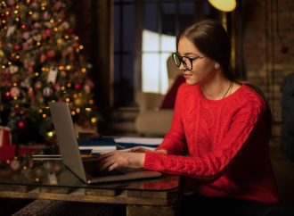 A young woman at a laptop and Christmas tree in the background