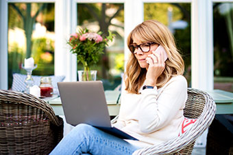 Portrait of middle aged woman using laptop and talking with somebody on her mobile phone while working in the garden.