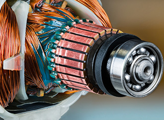 Closeup of ball bearing, commutator and rotor and stator inside electric DC motor. Copper wire with green epoxy in detail of machine to convert electrical energy into mechanical.