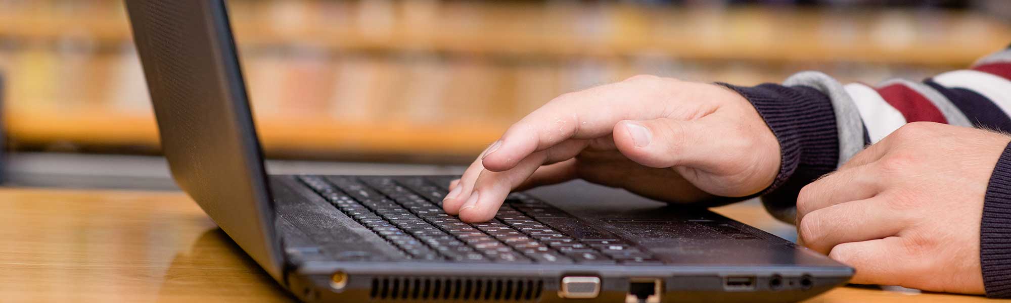 Hands typing on laptop in library