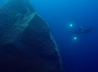 A large rock in the sea and a diver approaching it