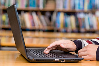Hands typing on laptop in library