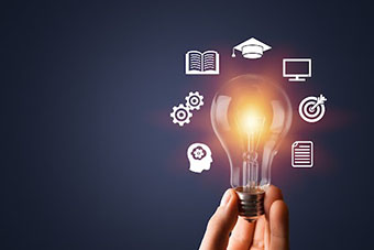 A bulb in a hand with icons, that refer to education, around the bulb