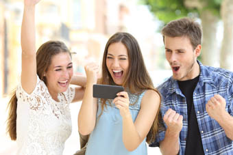 Three students celebrating whilst looking at a smartphone