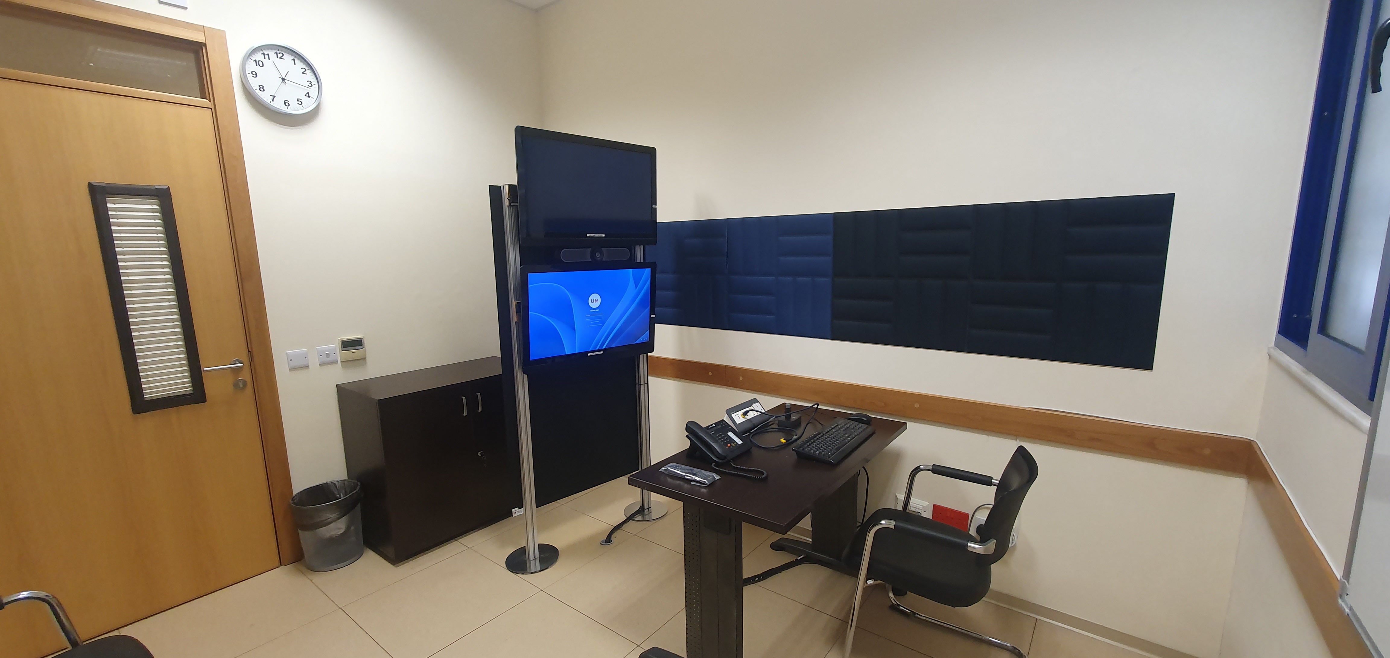 A small lecture capture space with a desk and computer, guest seating, a whiteboard, and walls lined with acoustic foam squares.