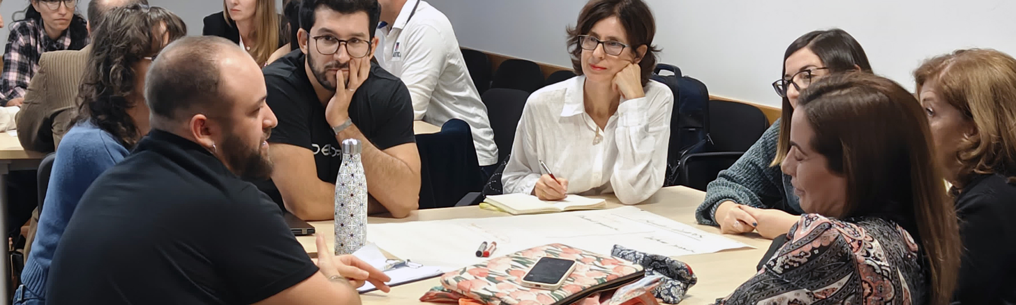 A workshop in session with groups of people discussing at different tables in a lecture room