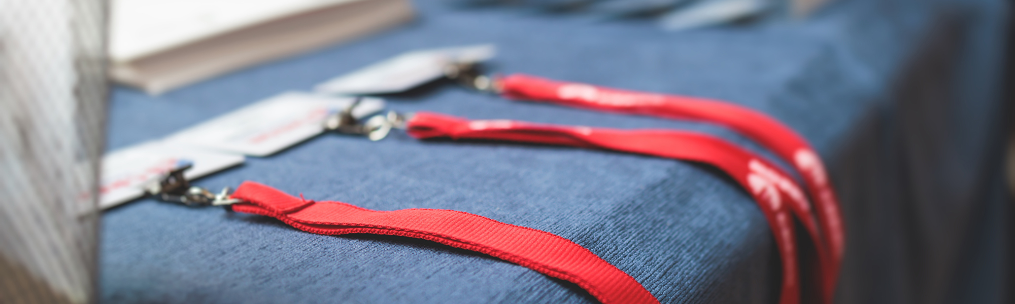 Close-up of red lanyards with name badges laid out on a blue-covered registration table, prepared for event or conference attendees.