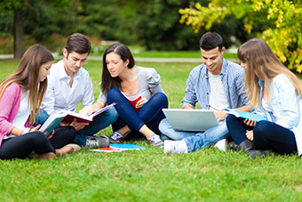 Students chatting, with books and laptops, sitting on grass