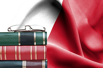 Education concept - Stack of books and reading glasses against National flag of Malta