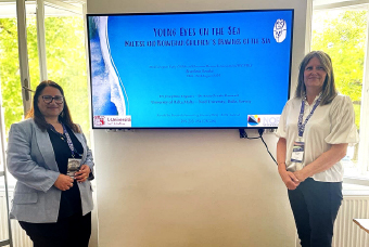 Two academics standing beside a screen displaying a presentation