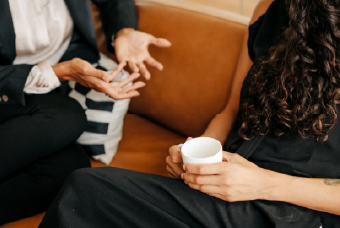 Two people talking on a sofa, one holding a coffee cup