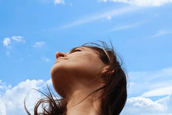A person looking up towards the sky with clouds in the background