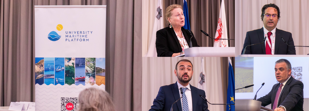 On the left hand side of the picture, the conference banner in the conference hall. On the other side of the picture, four speakers at during a conference in session,