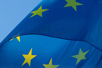 The EU flag - a blue flag with yellow stars - against a blue sky backgroung