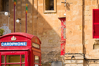 A red telephone box in a street with a building at the back