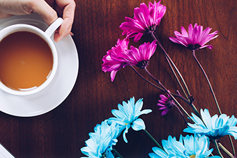 A hand holding a cup of tea and some flowers on a table