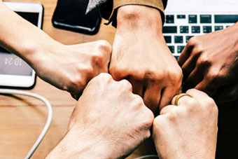 Five clutched hands denoting team spirit, a keyboard, smartphones on a desk