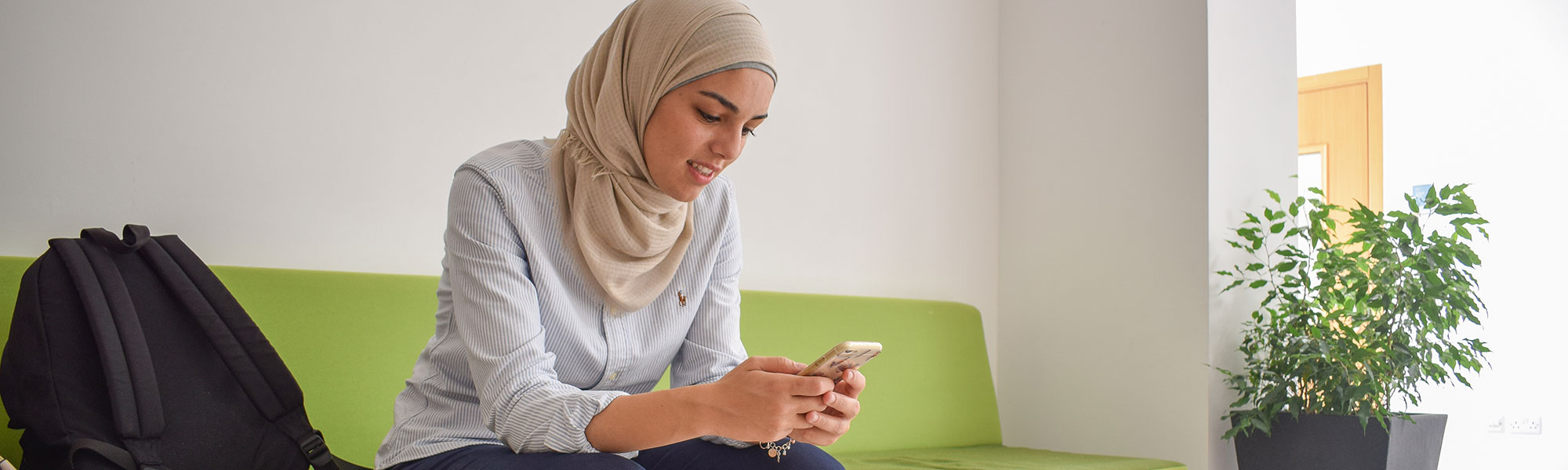 International student seated on green couch and looking at mobile phone